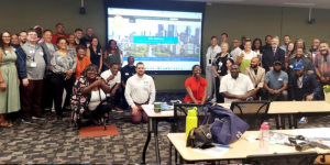 Philadelphia Peer Support Gathering. Large group split into two sections standing on both sides of a screen showing the Peer Institute website.